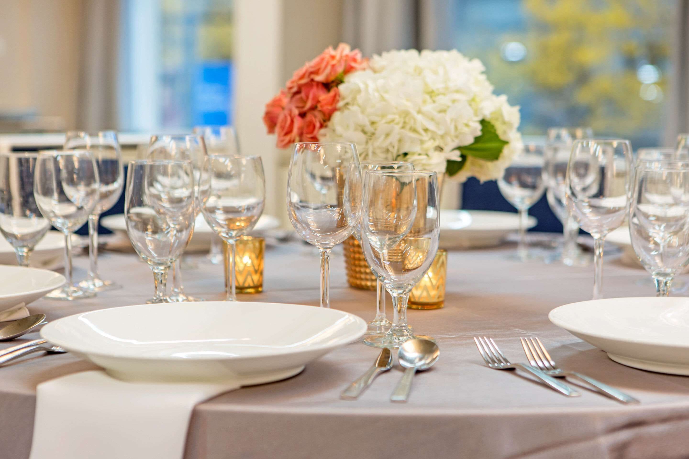 A table set for a formal dinner with white plates, silverware, and clear wine glasses.