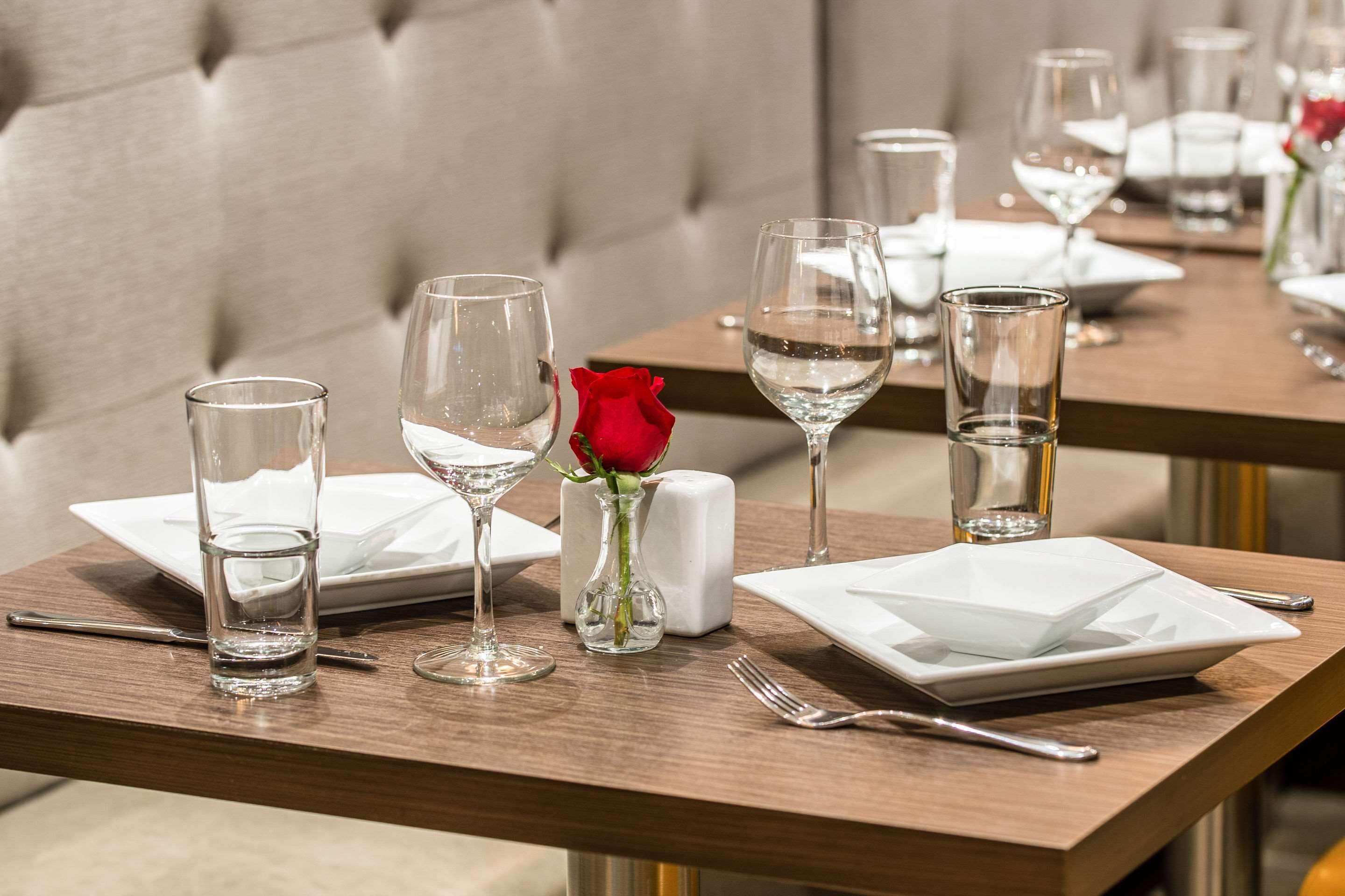 A dining table set with glasses, a rose, and a salt shaker.