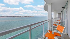 A balcony with white railings and orange chairs, overlooking a body of water and a distant shoreline. - Cambria Hotel Ocean City - Bayfront (Ocean City)