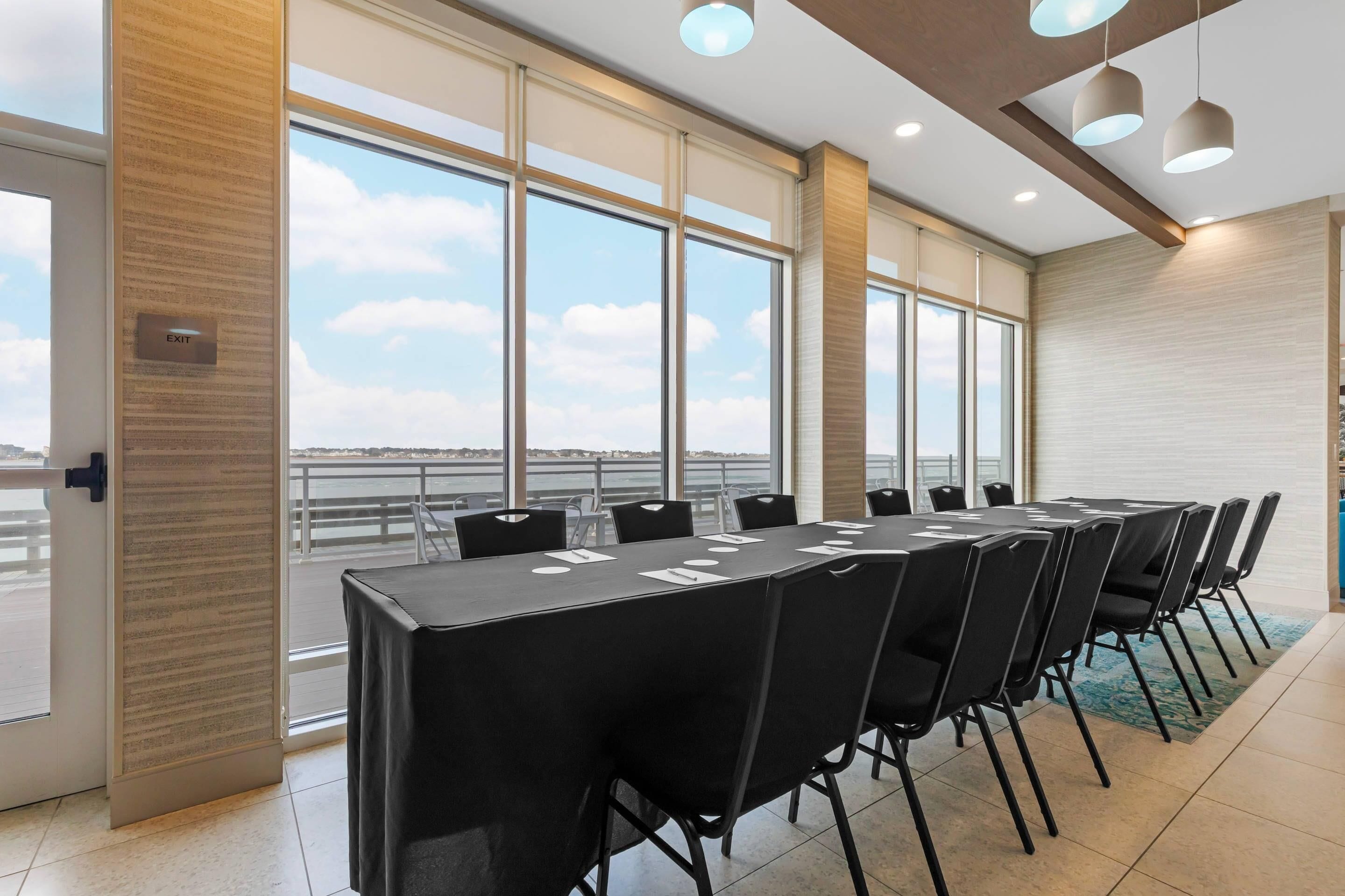 Un salón de conferencias con una larga mesa, sillas y ventanas amplias con vistas a un cuerpo de agua.