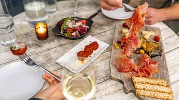 A dining table with various dishes, including a plate of prosciutto, a bowl of salad, and a glass of white wine.