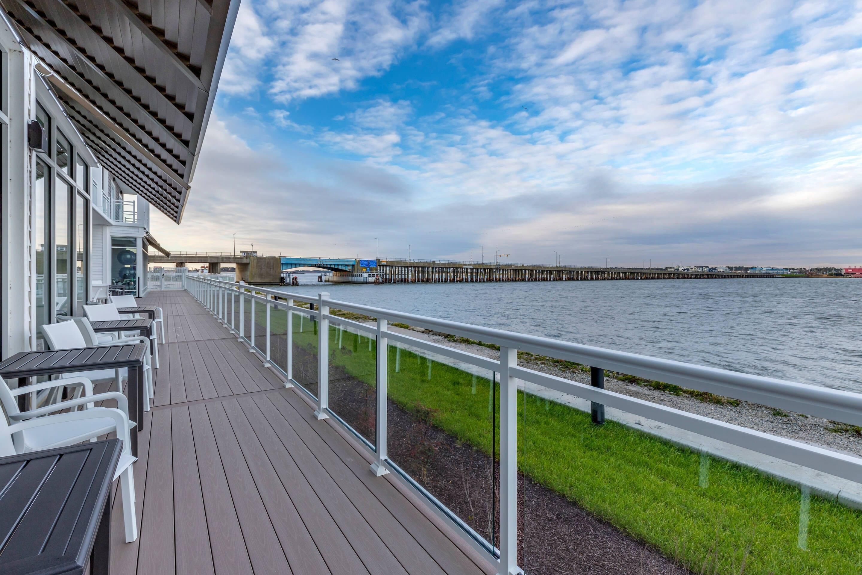 A deck with outdoor seating, a railing, and a view of a pier and water.