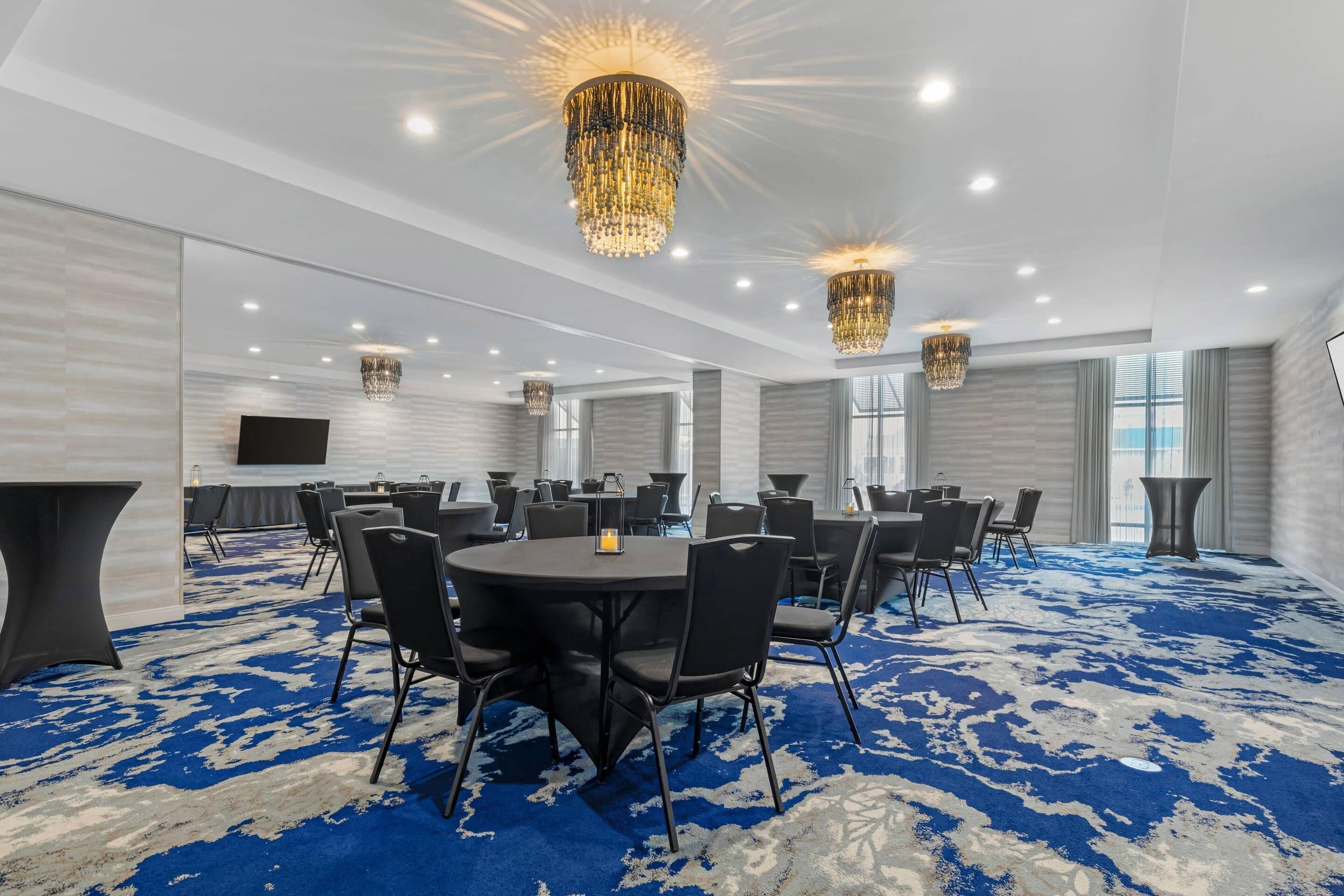 Un salón de conferencias con mesas redondas, sillas negras y una alfombra azul estampada.