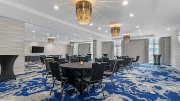 Un salón de conferencias con mesas redondas, sillas negras y una alfombra azul estampada.