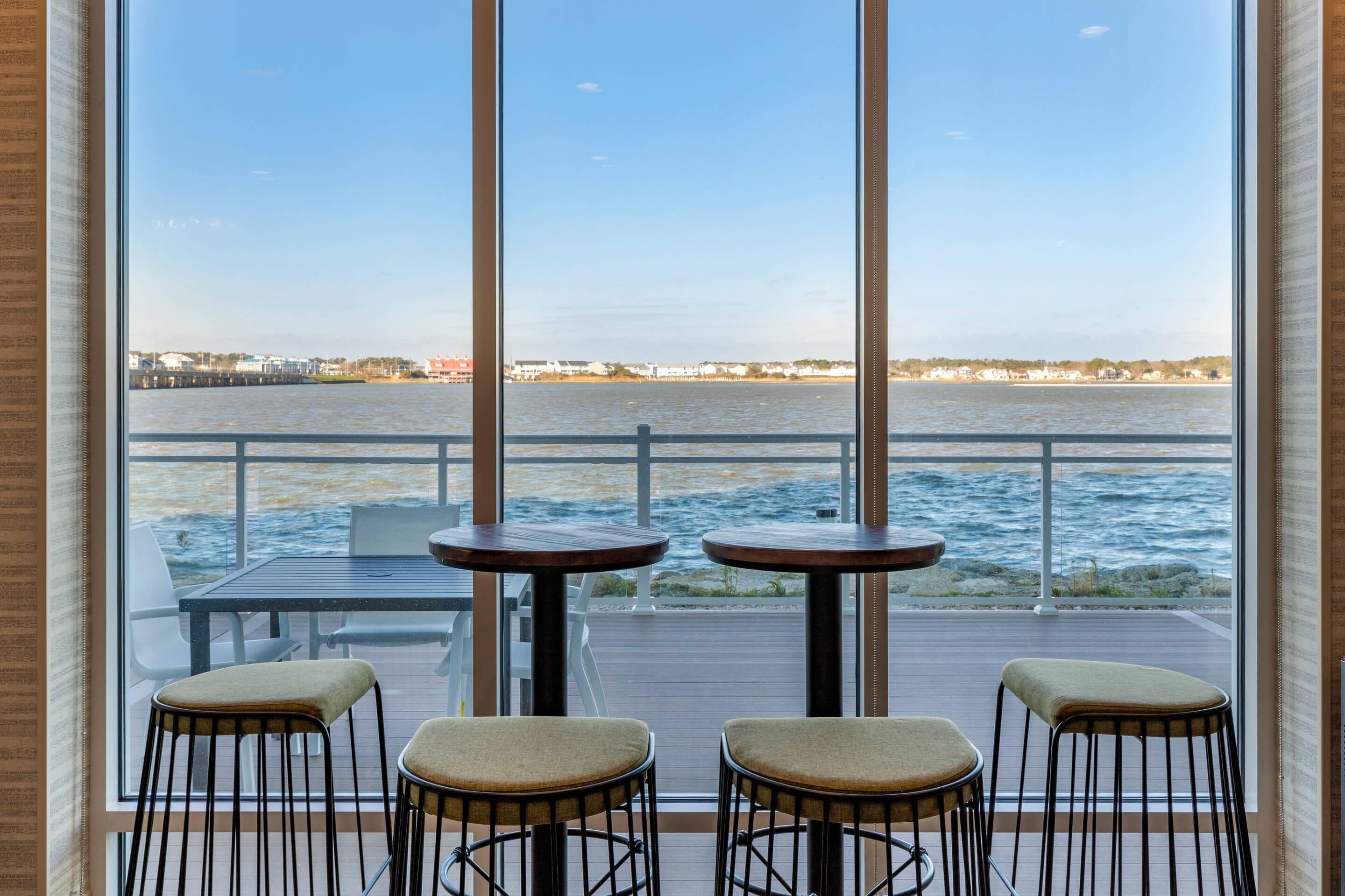 A deck with three tables and chairs, overlooking a body of water with a distant shoreline.