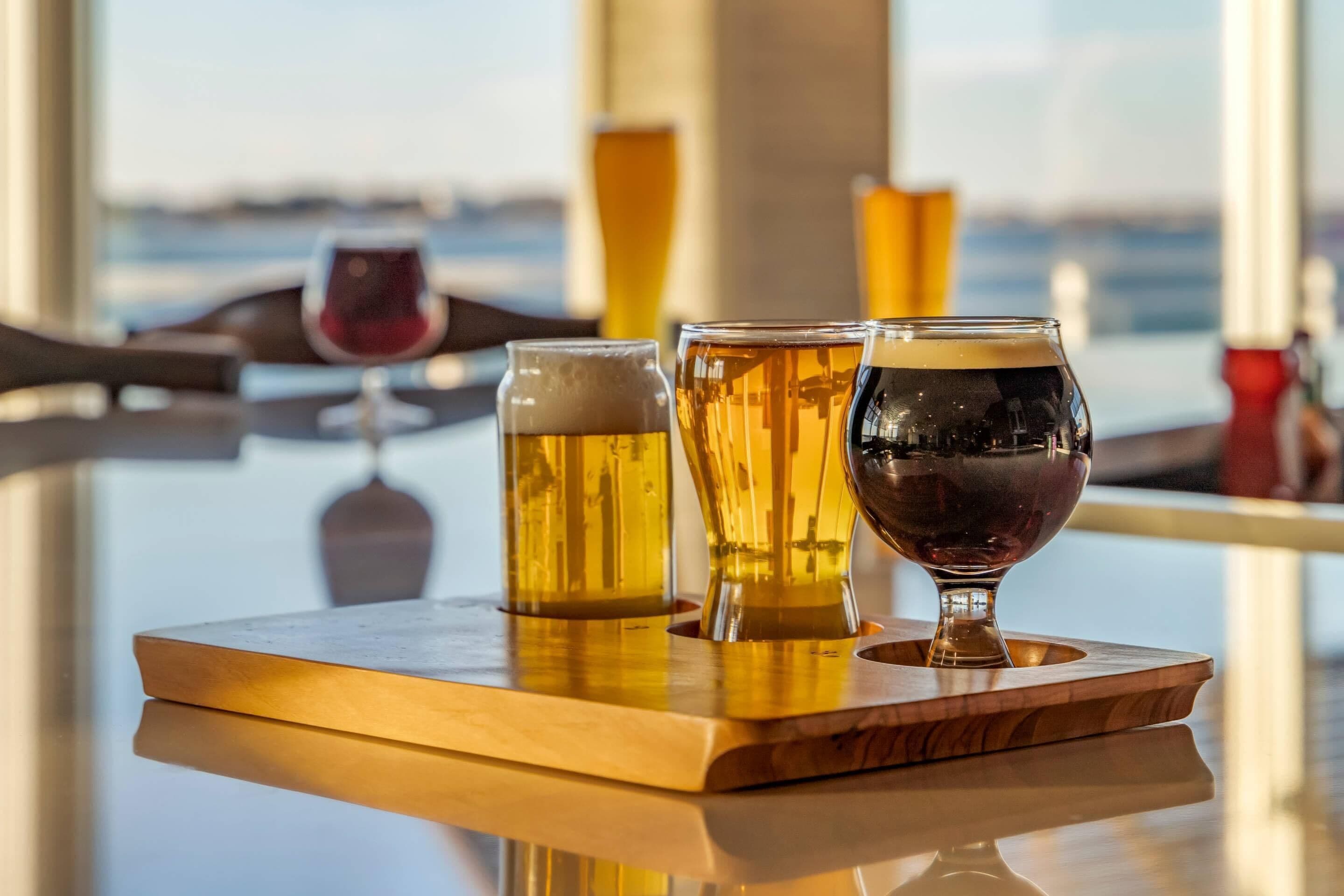 A bar setting with glasses of beer and a wine glass on a wooden tray.