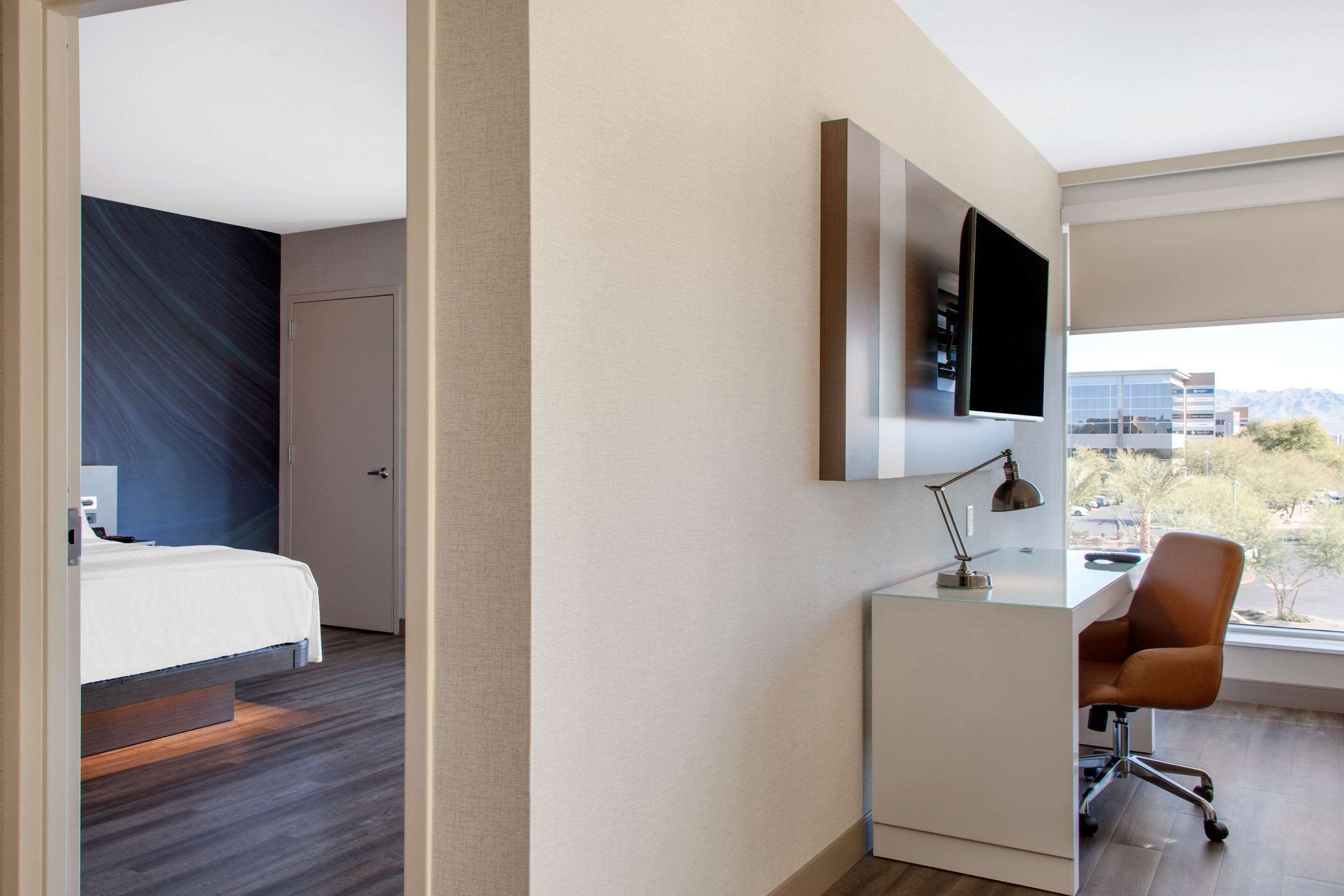 Una habitación de hotel moderna con una cama, un escritorio con una silla, un televisor montado en la pared y una ventana con vista a la ciudad.