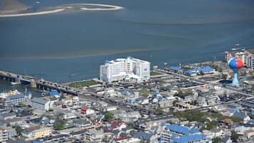 Vista aérea de un pueblo costero con un edificio blanco destacado de techo azul, una torre de agua azul y roja, y un puente que lo conecta a tierra firme.