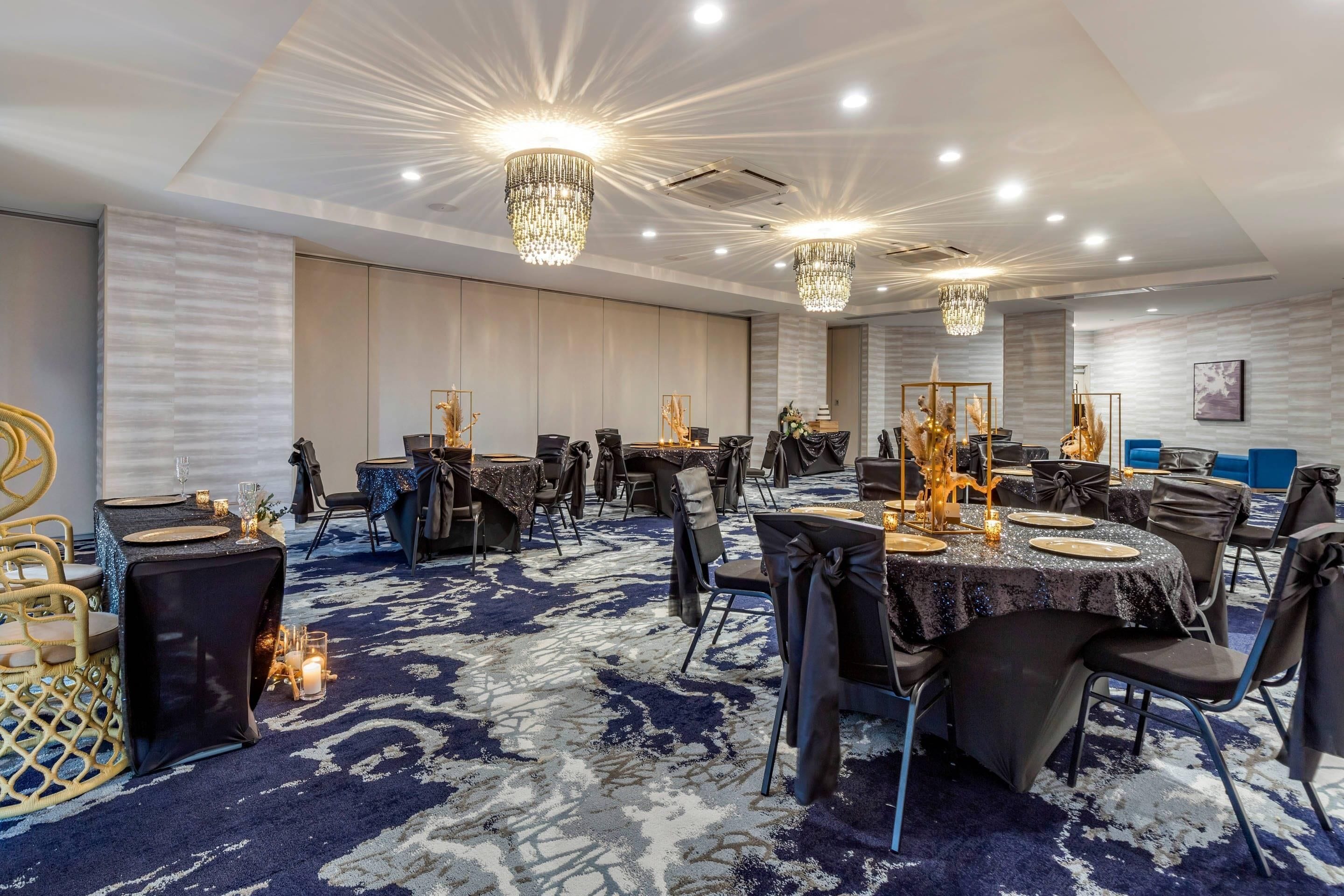 A banquet hall with round tables, chairs, chandeliers, and a patterned carpet.