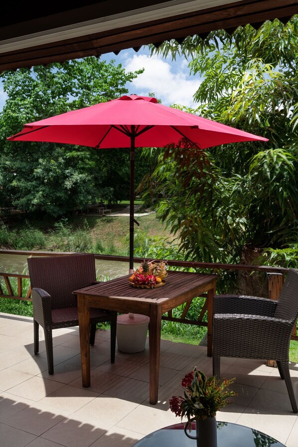 A patio with a table and two chairs, a red umbrella, and a potted plant with flowers.
