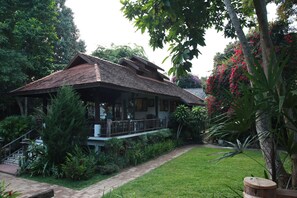 Una casa tradicional amb teules, envoltada de vegetació exuberànt i un jardí ben cuidat.