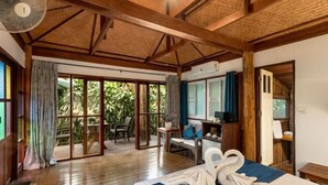 Une chambre avec un lit, un ventilateur, un bureau et une vue sur la verdure, accessible par une porte coulissante.