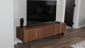 A wooden TV stand with a flat-screen TV, remote controls, and a cable box. - Fresh space near Mayo Clinic and downtown (Rochester)