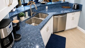 Eine Küche mit blauer Granitarbeitsplatte, Spüle aus Edelstahl und Geschirrspüler. Auf der Arbeitsfläche stehen eine Kaffeemaschine und ein Toaster.