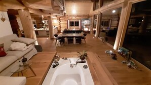 Interior de una cabaña de troncos con una bañera grande, piso de madera y un comedor.