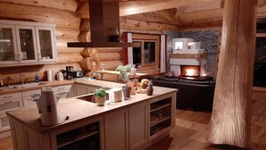 Interior de una cabaña de troncos con una isla central, armarios de madera, una chimenea de piedra y una zona de estar acogedora.