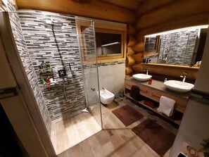 Un baño moderno con cabina de ducha de vidrio, un bidé y un lavabo doble.