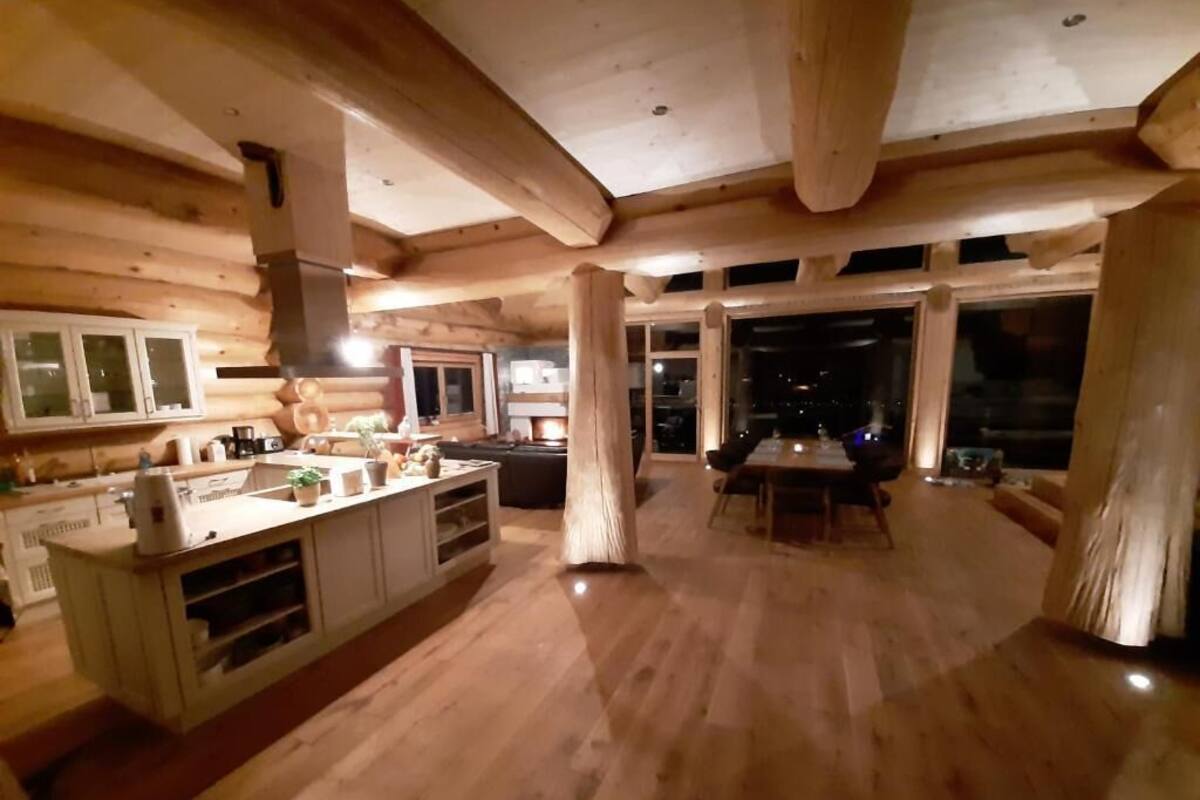 Ein Holzblockhaus-Innenraum mit Küche, Essbereich und großen Fenstern.