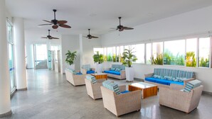 A spacious lobby with multiple seating areas, ceiling fans, and large windows offering views of greenery. - Ocean Front Apartment in Bocagrande (Cartagena)