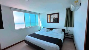 A hotel room with a bed, a window with a view of the sea, a painting on the wall, and a bedside table with a lamp. - Ocean Front Apartment in Bocagrande (Cartagena)