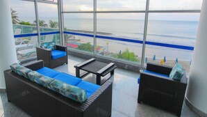 A balcony with wicker furniture, a view of the ocean, and a beach in the background. - Ocean Front Apartment in Bocagrande (Cartagena)
