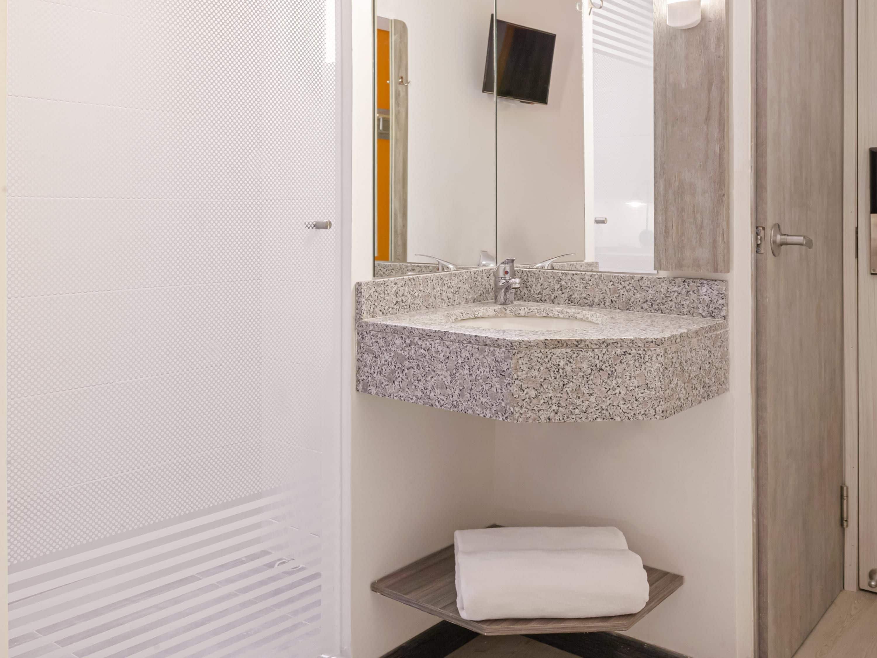 A bathroom with a granite sink, a mirror, a towel on a shelf, and a wooden door.