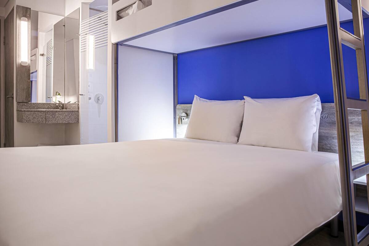 A modern hotel room with a large bed, a bathroom with a mirror, and a blue accent wall.