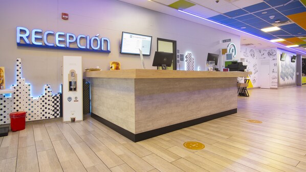 A reception area with a wooden reception desk, a digital screen, and a sign that reads "RECEPCIÓN". - ibis budget Barranquilla (Barranquilla)