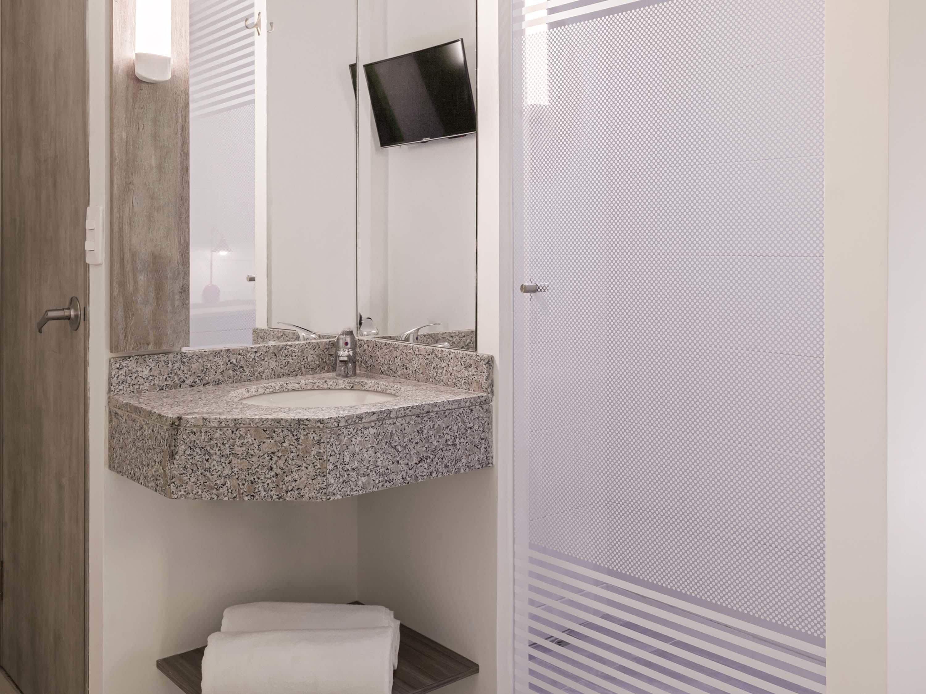 Un baño con lavamanos de granito, un espejo, inodoro y zona de ducha.