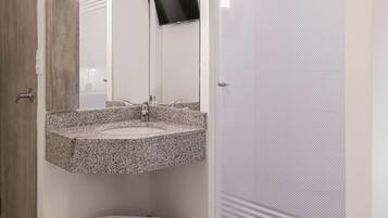 Un baño con lavamanos de granito, un espejo, inodoro y zona de ducha.
