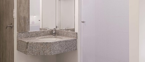 Un baño con lavamanos de granito, un espejo, inodoro y zona de ducha.