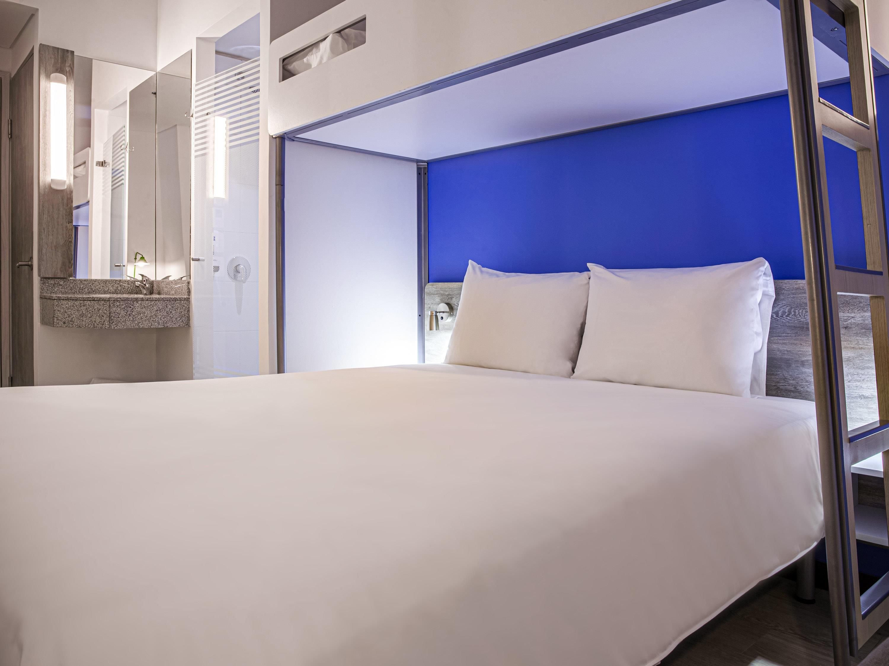 Una habitación de hotel moderna con una cama grande, un baño con espejo y una pared de acento azul.