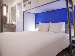 Una habitación de hotel moderna con una cama grande, un baño con espejo y una pared de acento azul.