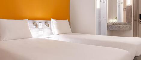 Habitación de hotel con dos camas, una pared de acento anaranjada brillante, un espejo grande y una encimera de granito.