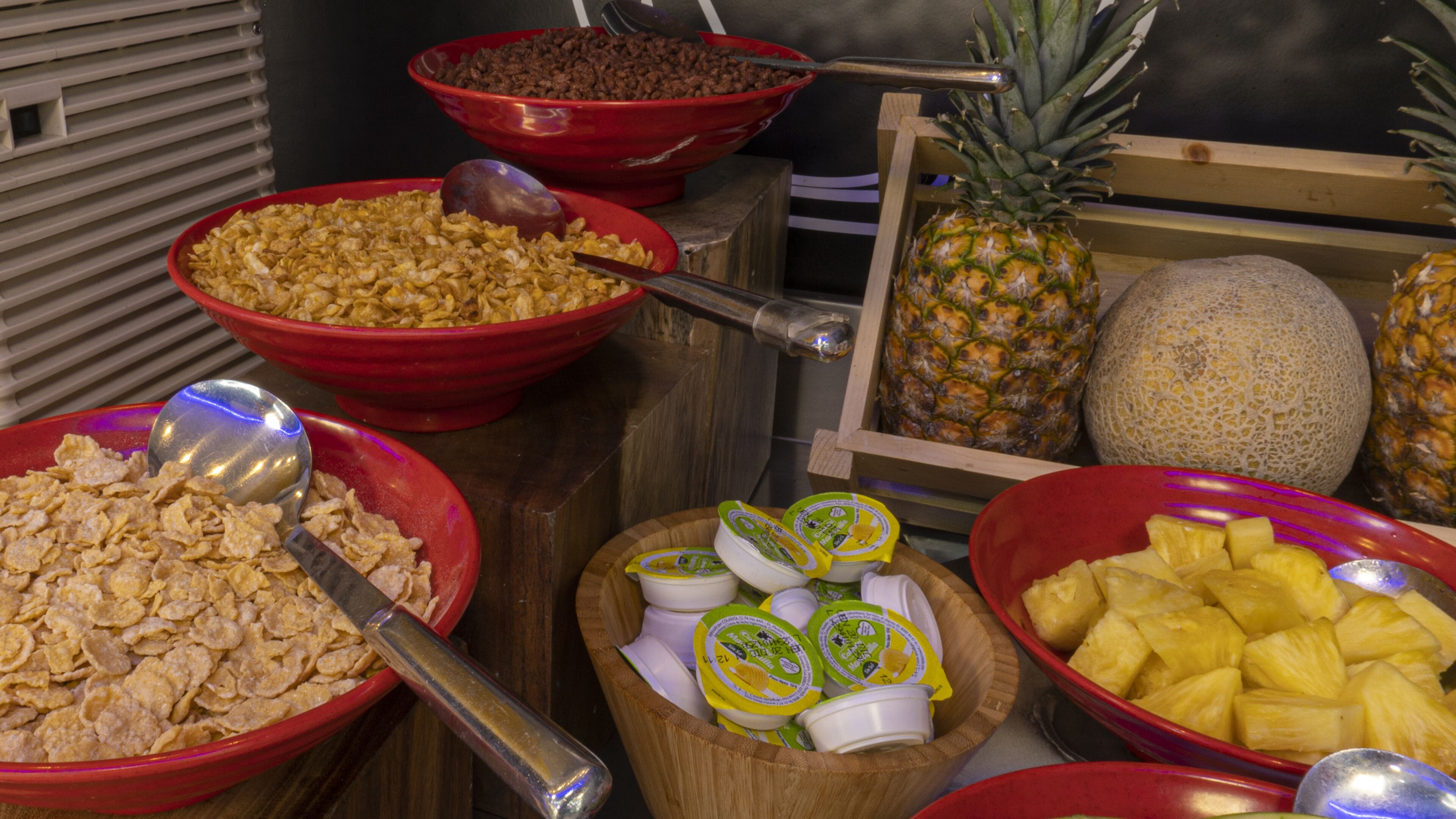 Une table de buffet proposant divers aliments, notamment des céréales, du yaourt, de l’ananas et d’autres fruits.
