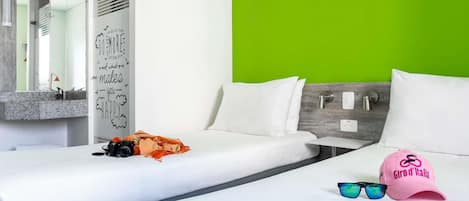 Une chambre d’hôtel avec deux lits, un mur d’accent vert, un miroir et un luminaire fixé au mur.