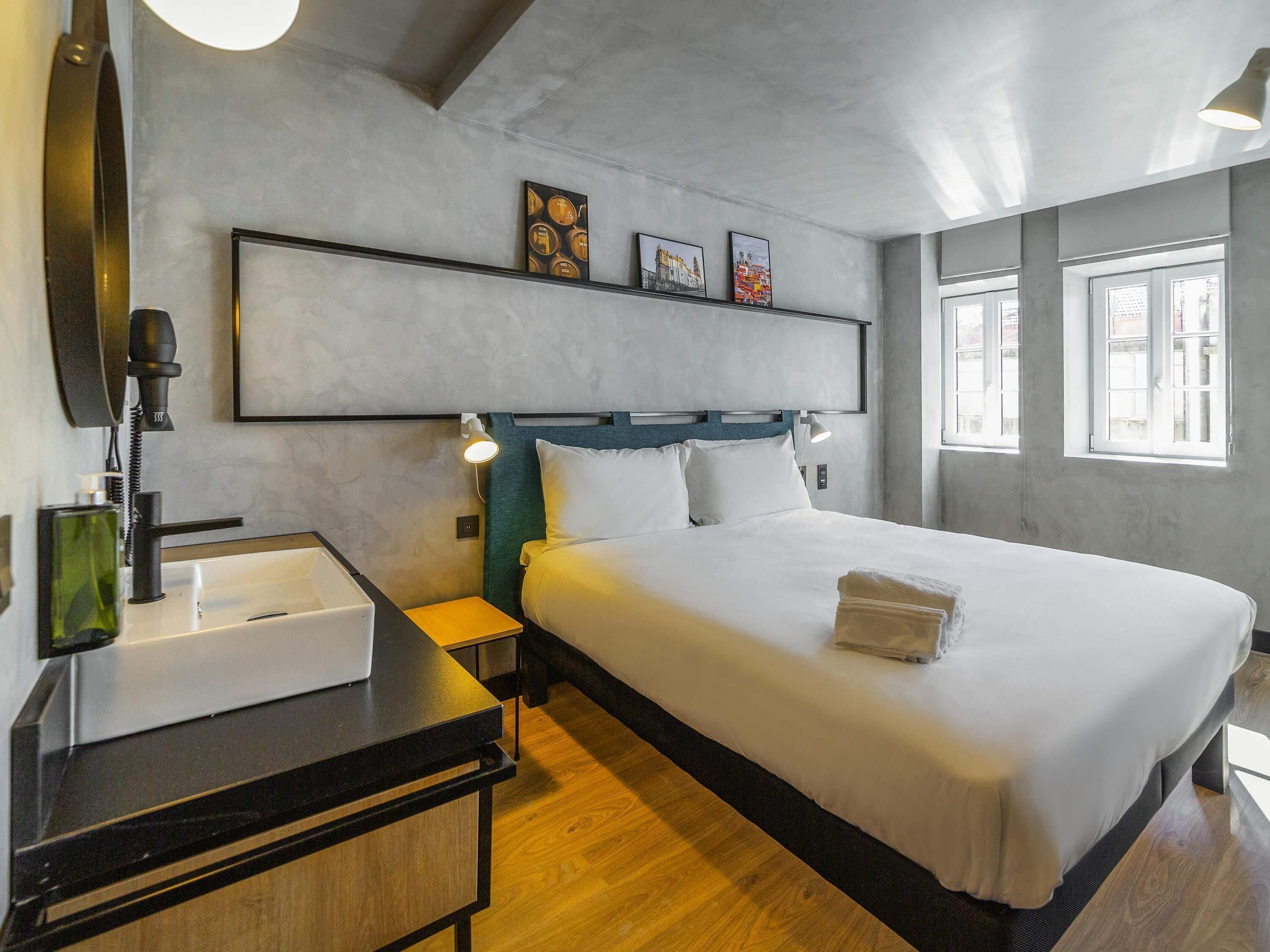 Una habitación de hotel con cama, mesita de noche, lámpara y una obra de arte en la pared.