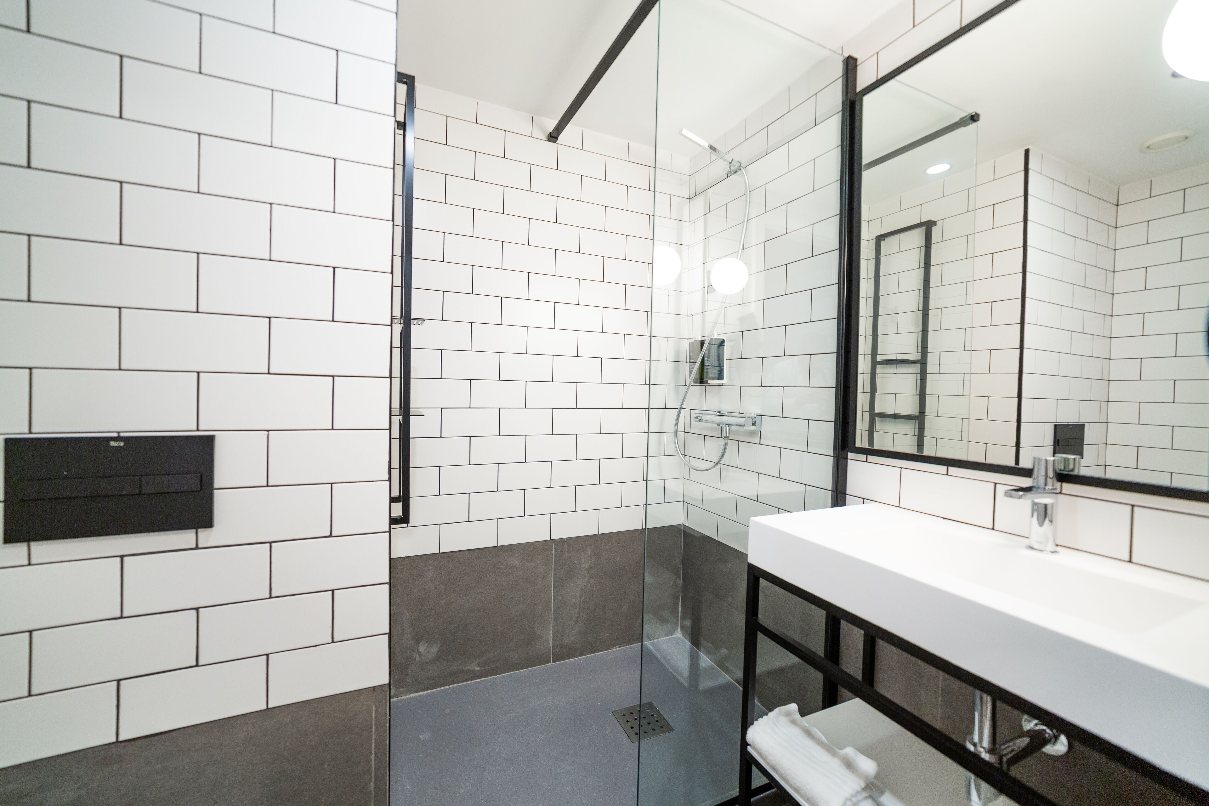 A modern bathroom with white and gray tiles, a glass shower enclosure, and a white sink with a black frame.