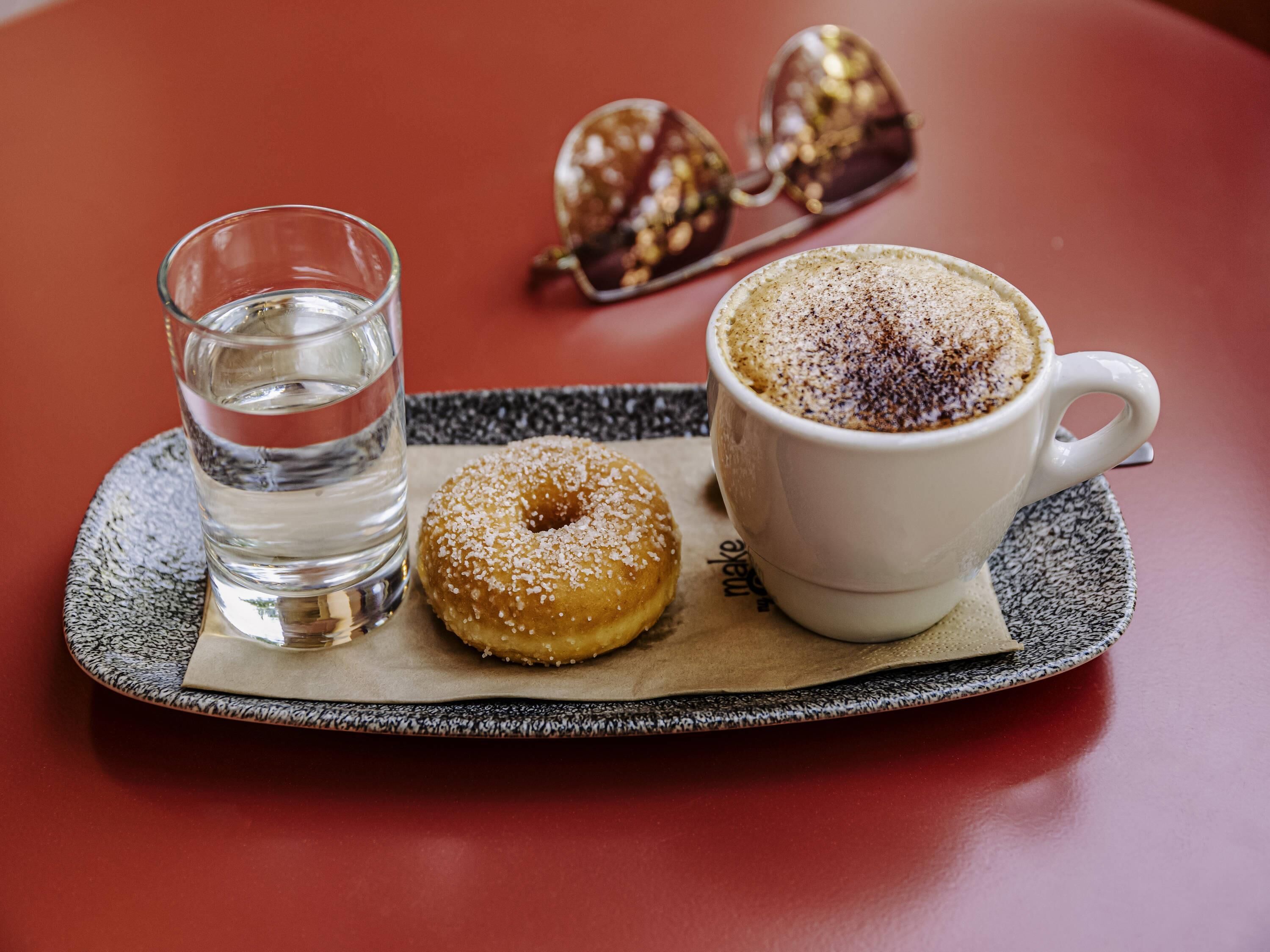 A tray with a glass of water, a donut, and a cup of coffee on a red table.