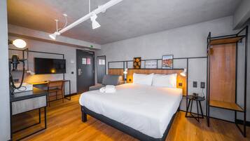 A modern hotel room with a large bed, a desk with a chair, a small table, and a TV.