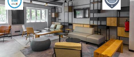 A modern hotel lobby with a clean and safe environment, featuring a sofa, chairs, a wooden bench, and a TV mounted on the wall.