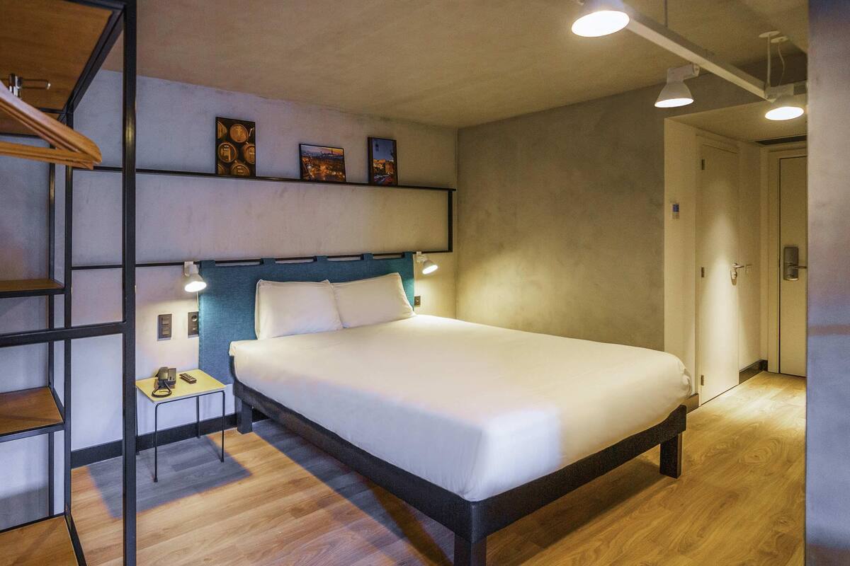 Een moderne hotelkamer met een groot bed, een bureau met telefoon en een plank met ingelijste foto's.