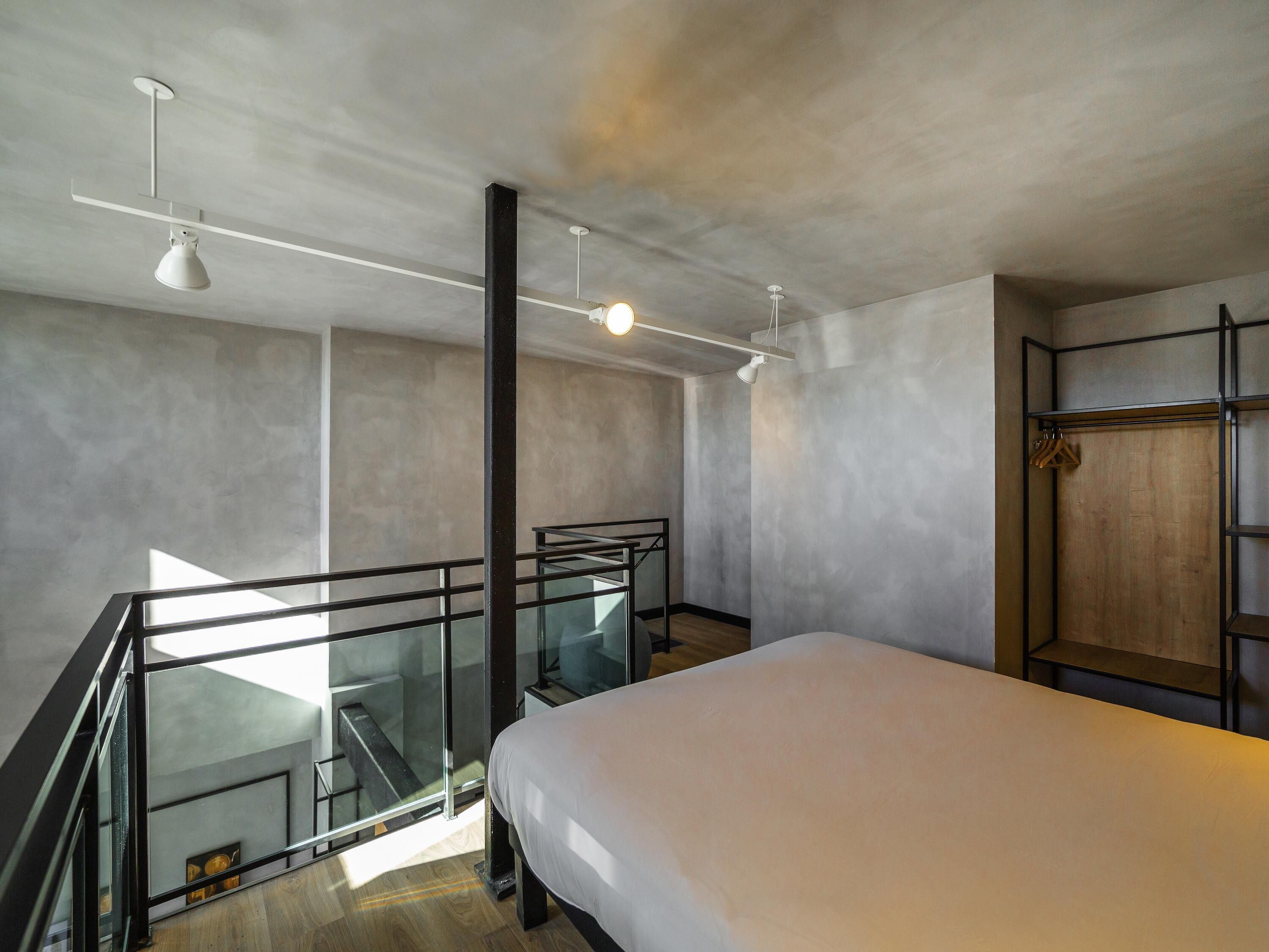 Un dormitorio moderno con una cama, barandilla de vidrio, armario de madera y una escalera.