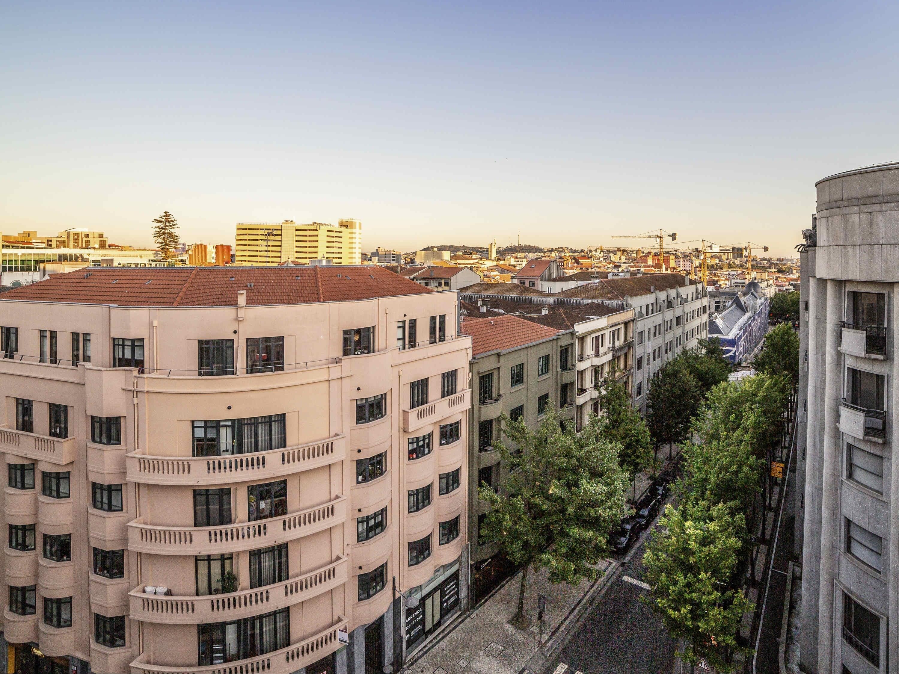 A multi-story building with balconies, a street with cars, and other buildings in the background.
