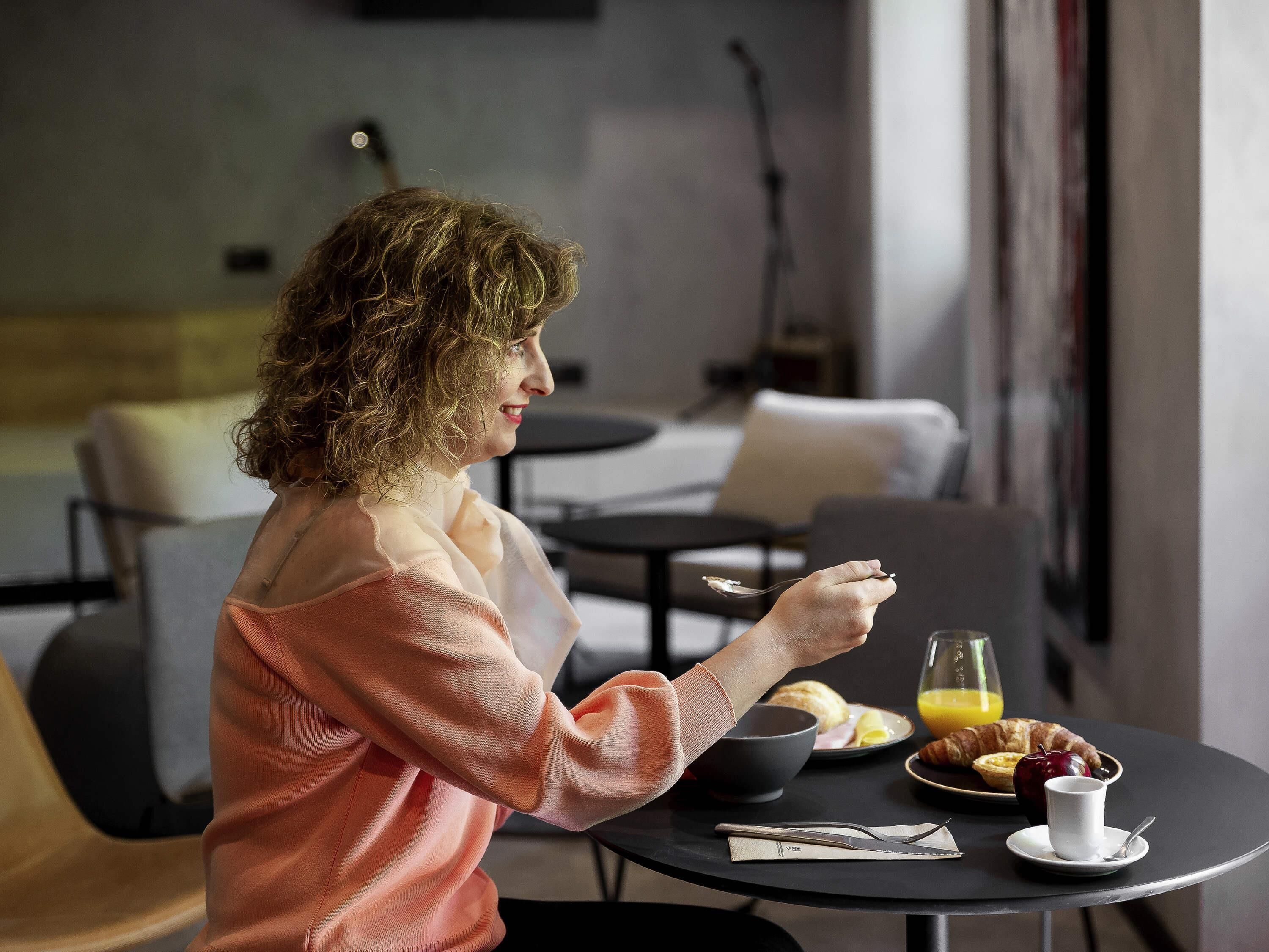 A person sitting at a table with breakfast items including croissants, a bowl, and a glass of orange juice.