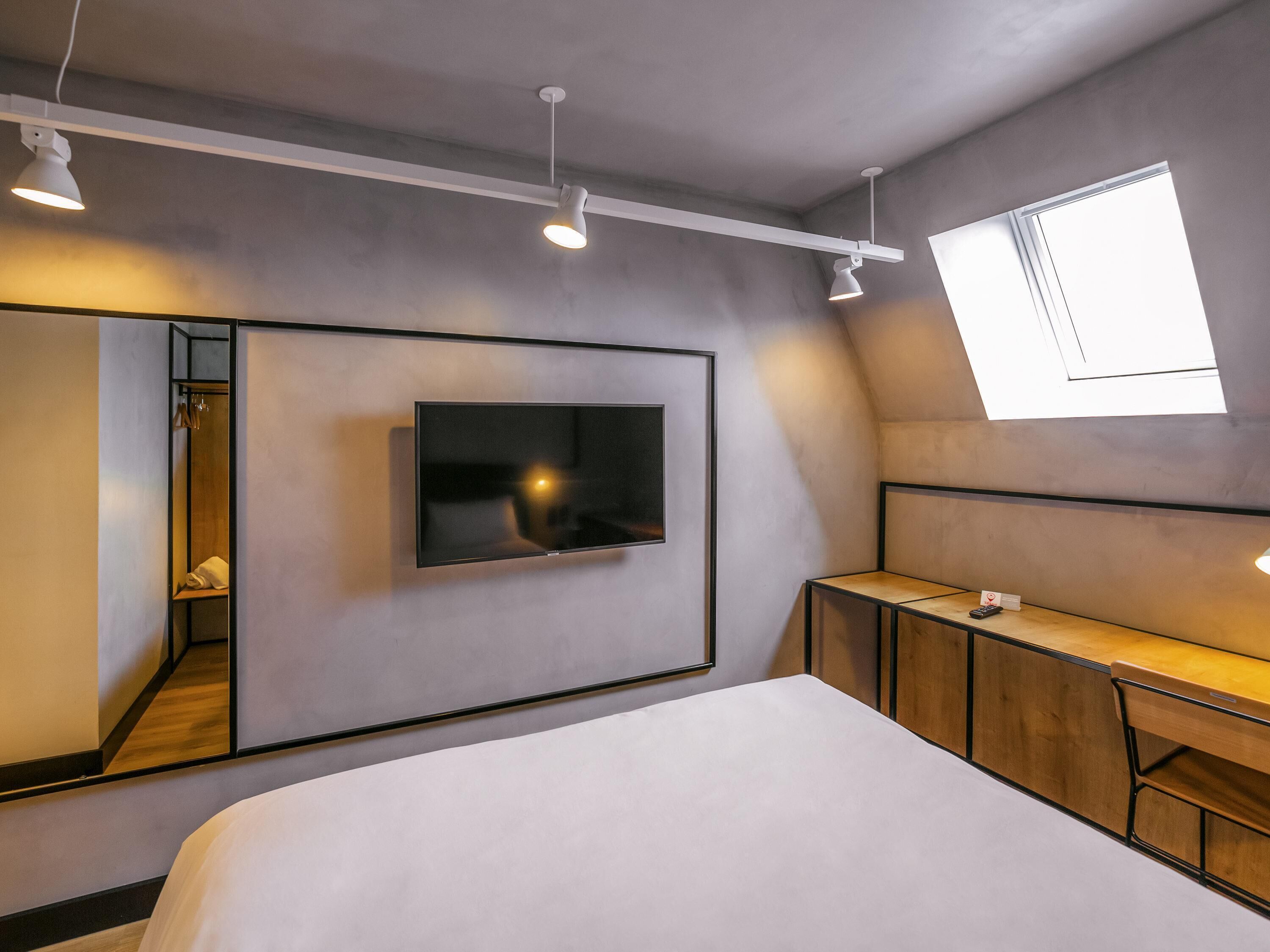 A modern bedroom with a large bed, a mounted TV, a wardrobe, and a skylight.