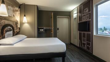 Una habitación de hotel moderna con cama, televisor de pared, armario y un gran ventanal.