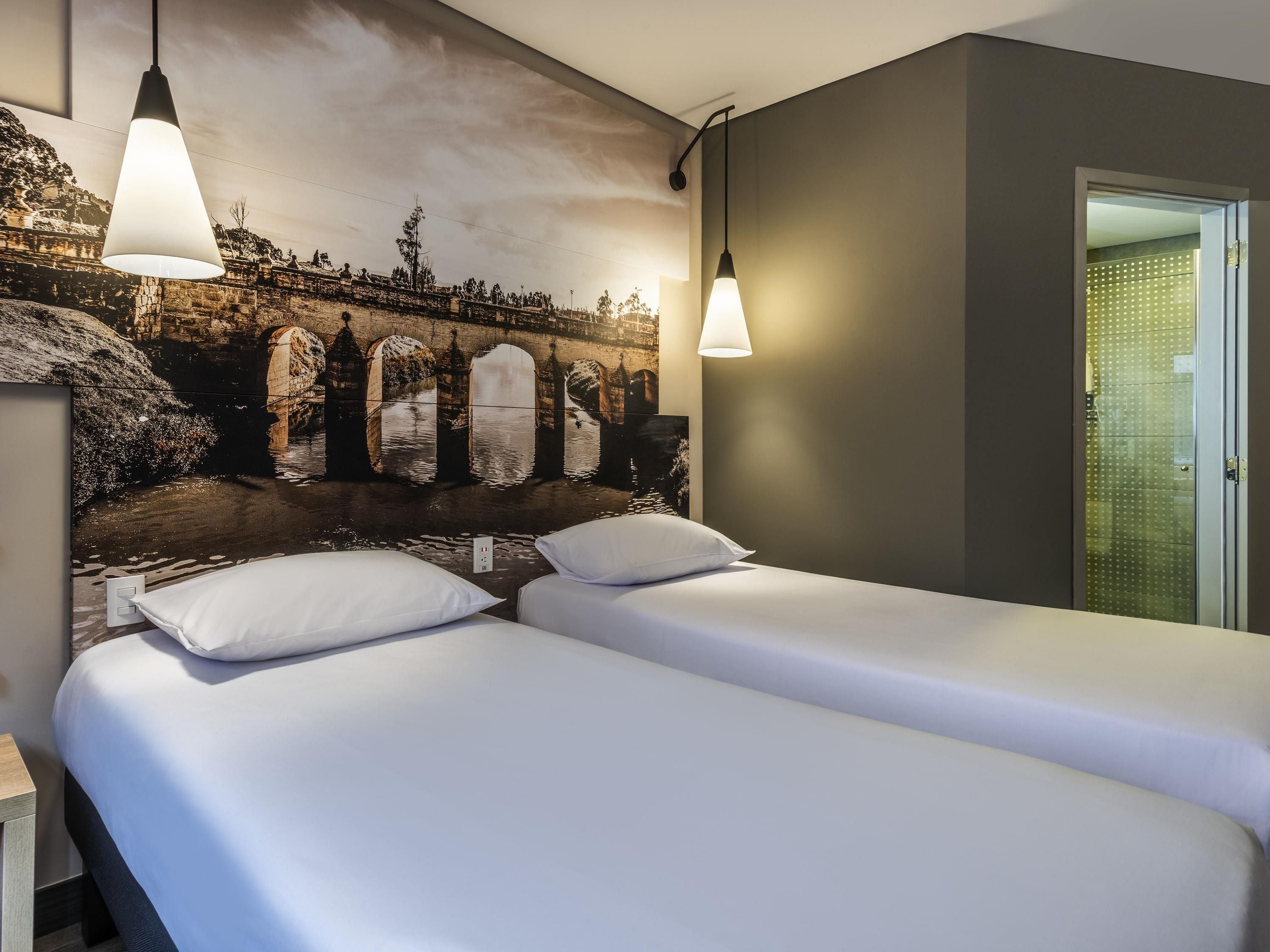 Habitación de hotel con dos camas, un mural de un puente y lámparas colgantes.