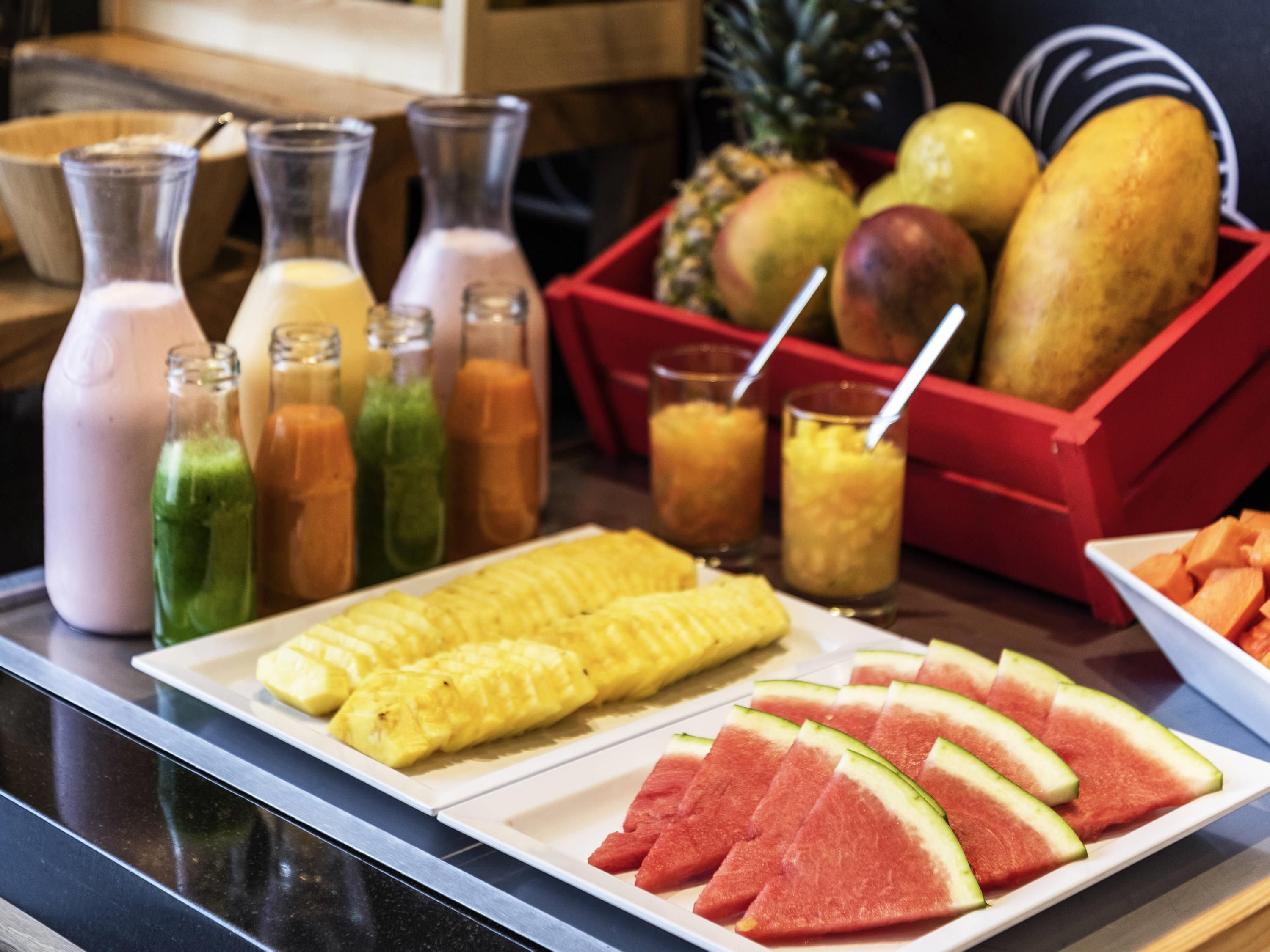 A buffet table with various fruits, a pineapple, and several bottles of beverages.