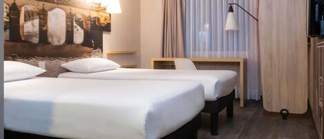 A hotel room with two beds, a desk, a chair, a TV, and a large window with curtains.